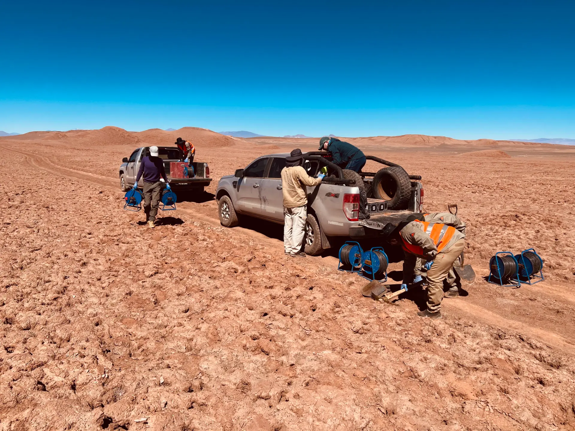 Crew unloading cable reels from pickups on a red salar surface
