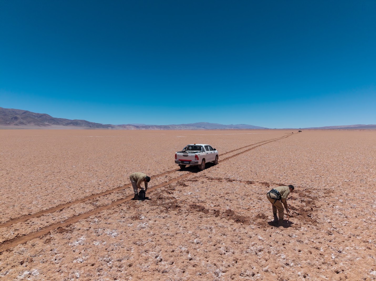 Two geophysicists setting electrodes along a track on an open salt flat